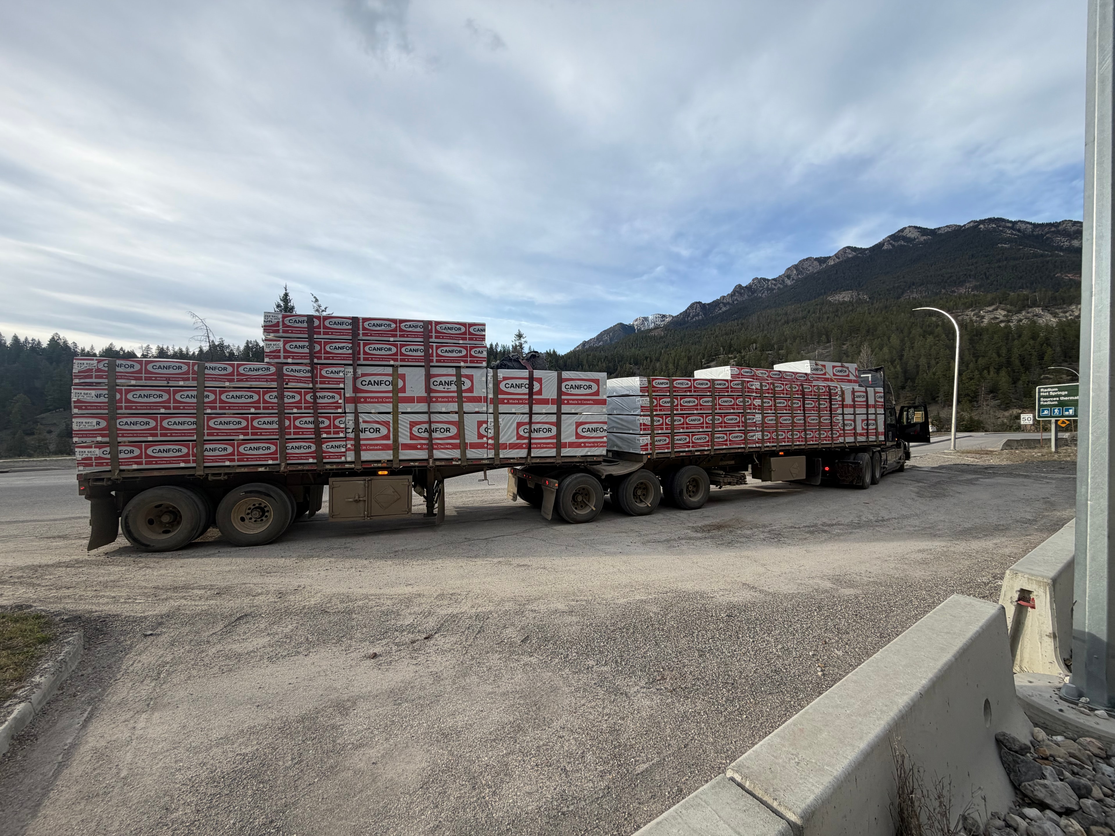 Flatbed truck hauling Canfor lumber through mountain landscape in Western Canada